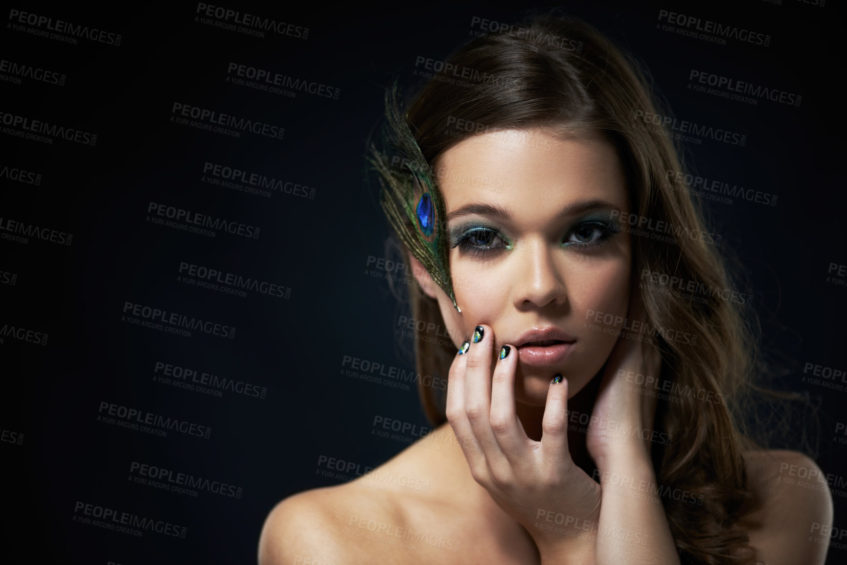 Buy stock photo Shot of a young brunette with peacock-themed makeup against a dark background
