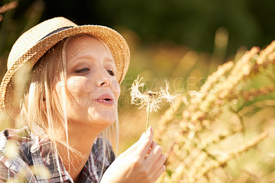 Buy stock photo Woman, blow flower and wish in nature with smile, wheat and grain in field, fun and playful in outdoors. Happy female person, freedom and fashion or hat, peace and joy on countryside vacation or trip