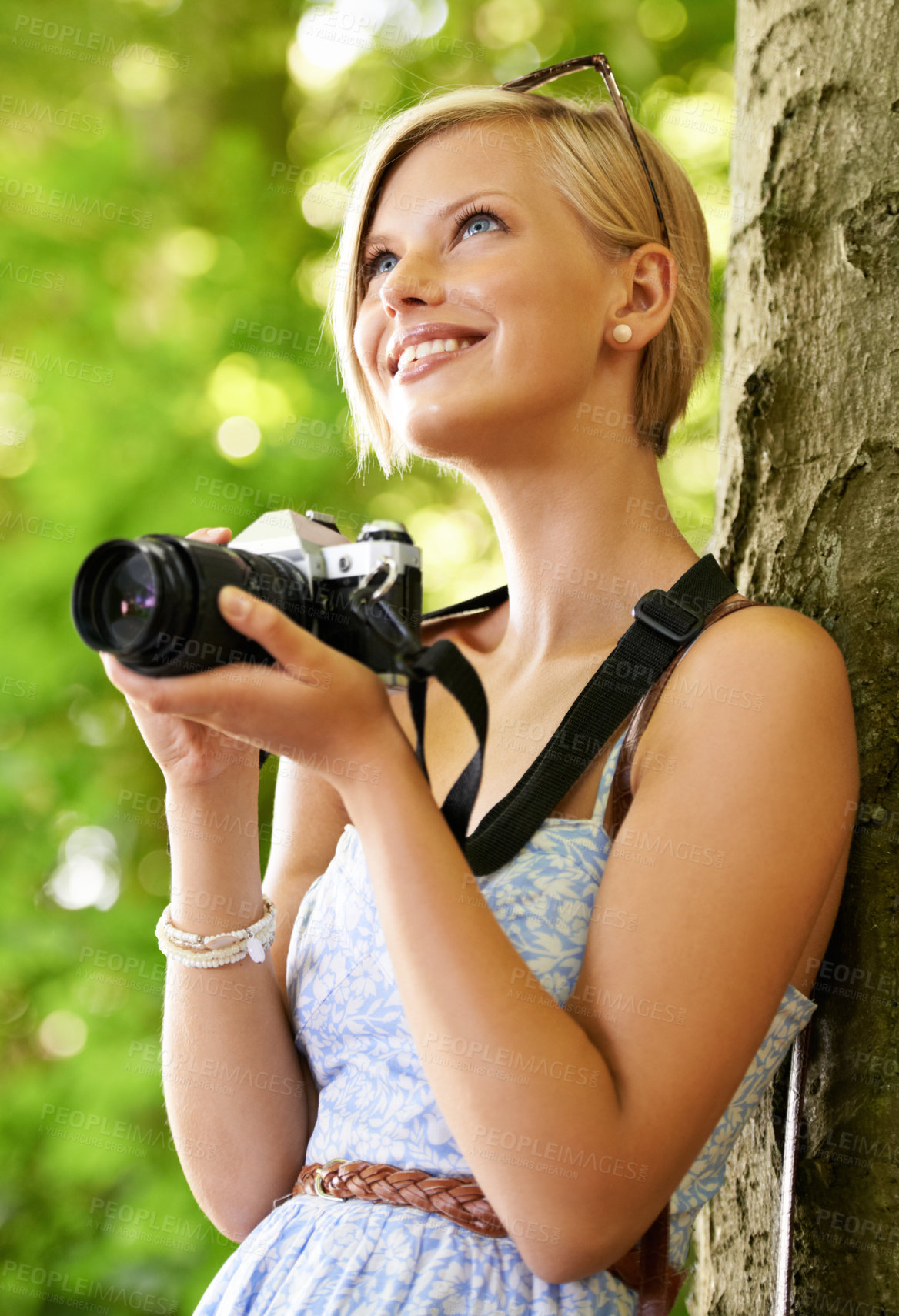 Buy stock photo Cute young photographer holding her camera and leaning against a tree