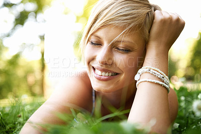 Buy stock photo Trendy and attractive young blonde woman lying on the grass outdoors with her hand in her hair