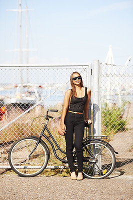 Buy stock photo A beautiful young woman standing in front of her bicycle at the harbour
