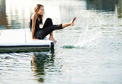 Buy stock photo A gorgeous young woman playfully kicking up water at the harbour