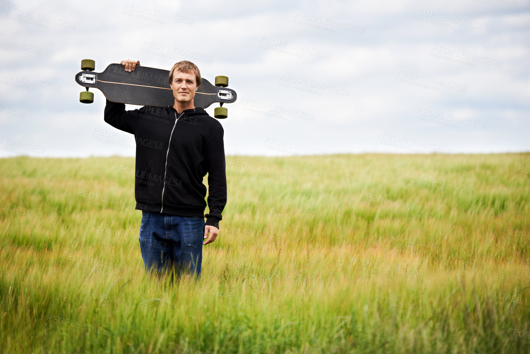 Buy stock photo Young skateboarder holding his board on his shoulder while standing in a field