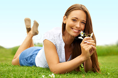 Buy stock photo Cute young woman smiling and holding a flower while lying on the grass