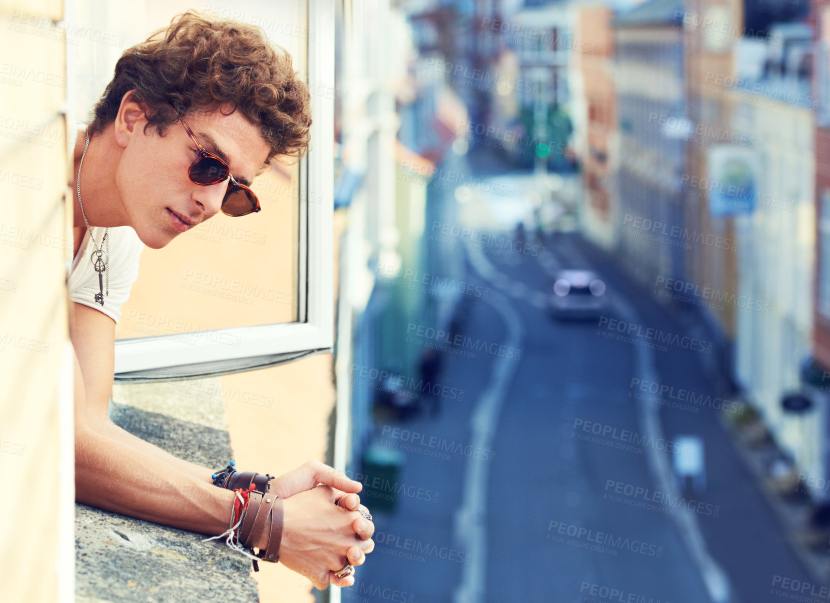 Buy stock photo A young man watching the street far below while leaning out of a window