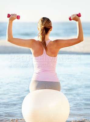 Buy stock photo Woman, pilates ball and sitting with dumbbell for fitness on beach, fresh air or peace. Female instructor, stretching or balance in back view for health, wellness or zen for meditation for outdoors