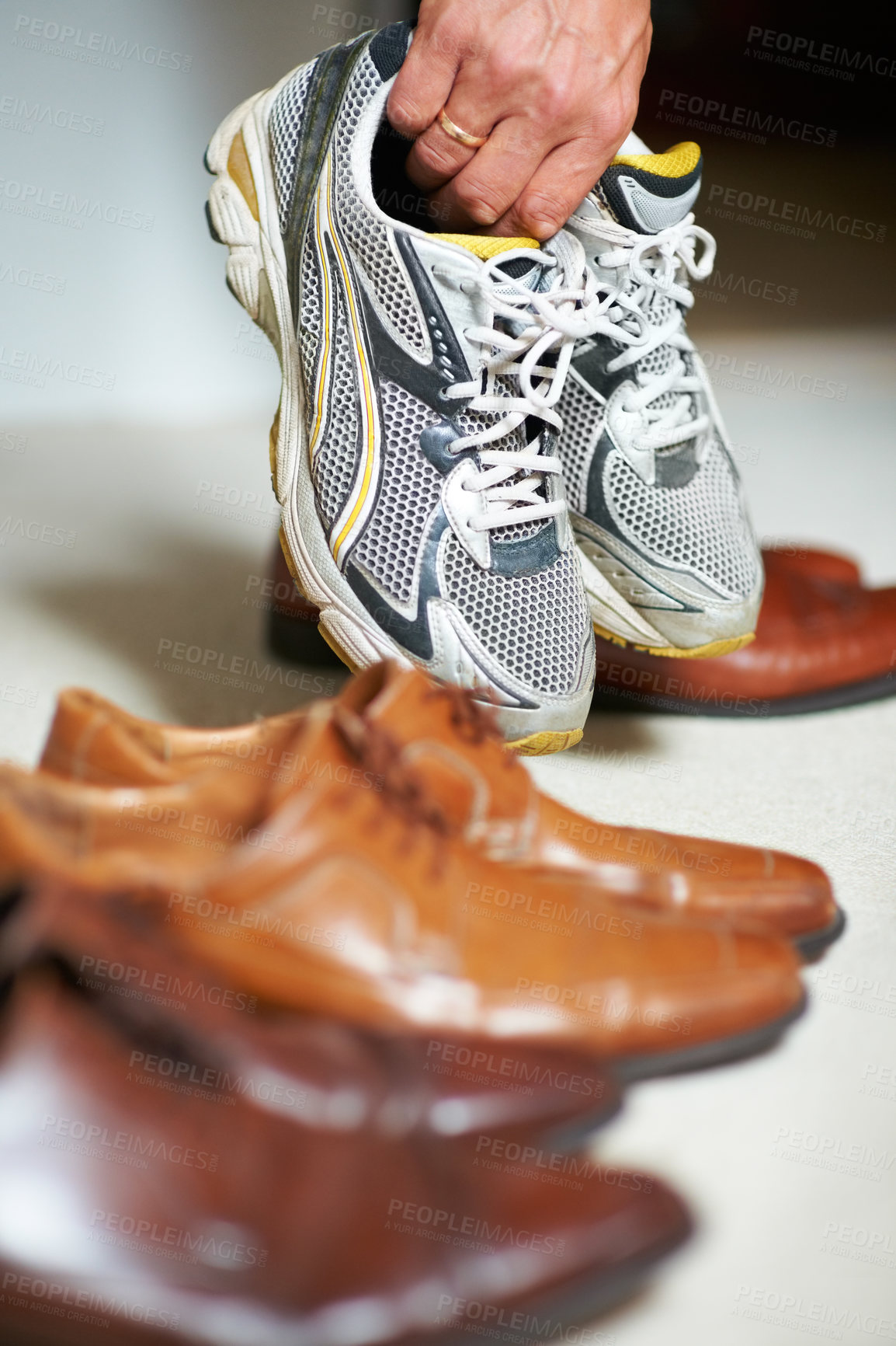 Buy stock photo Cropped shot of a man grabbing his running shoes from amongst his formal shoes