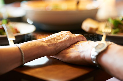 Buy stock photo Cropped shot of a couple holding hands in prayer at the table before eating