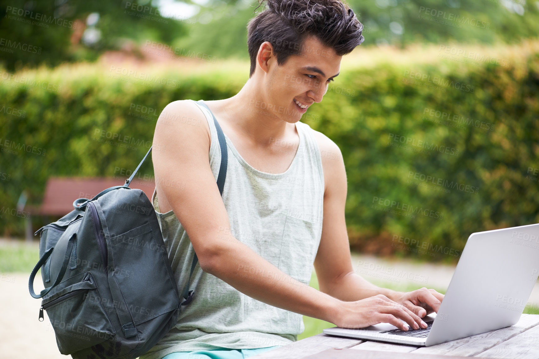 Buy stock photo A handsome young man typing on his laptop while sitting in the park