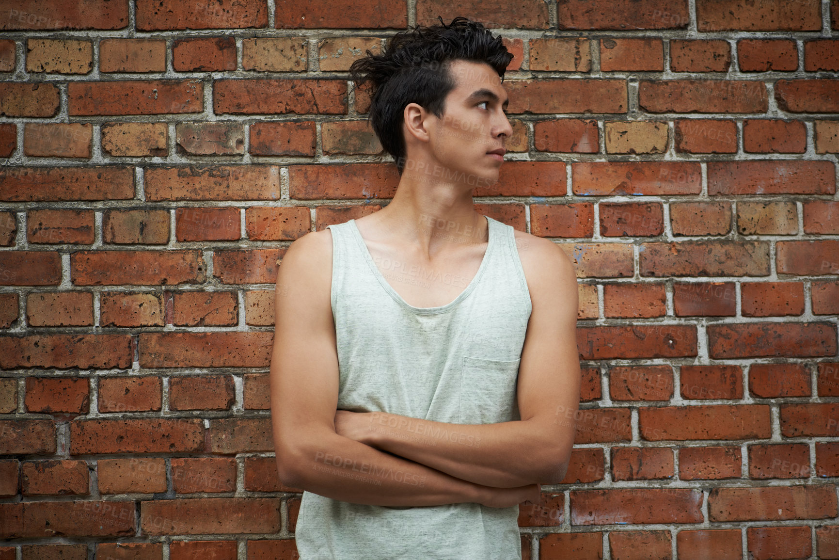 Buy stock photo A young man with crossed arms leaning against a brick wall