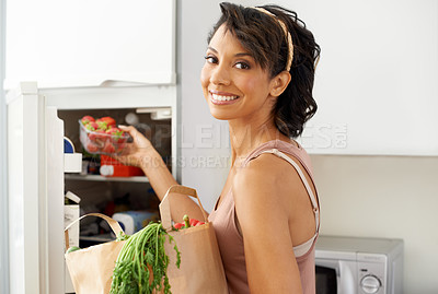 Buy stock photo Portrait of a young woman putting some fruit into a fridge