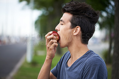 Buy stock photo A young man taking a bite of an apple while waiting for the bus
