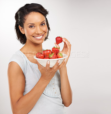Buy stock photo Portrait of a young woman enjoying a bowl of strawberries