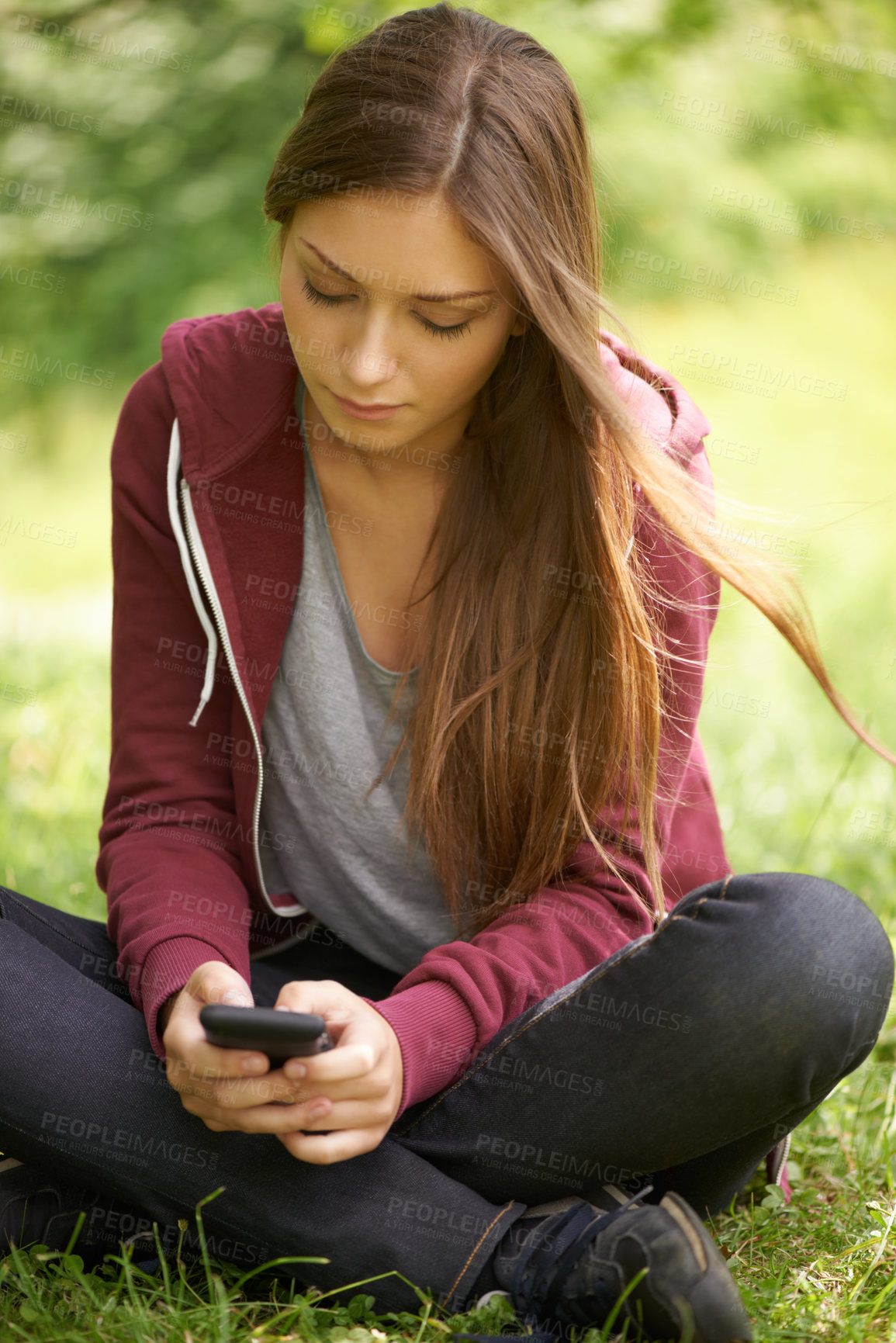 Buy stock photo A pretty young girl texting on her phone while sitting in a green field