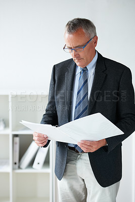 Buy stock photo Businessman, standing amd reading documents in office or company contract, report information or confidential file. Male person, suit or paperwork thinking or corporate agreement, decision or folder