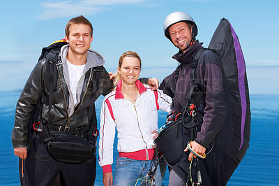 Buy stock photo Men, woman and portrait with happy for paragliding, extreme sport and outdoor by sea in sunshine. Group, fitness and smile on adventure with helmet, backpack or parachute for jump, safety or blue sky