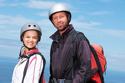 Buy stock photo Man, woman and portrait with smile for paragliding, extreme sport and outdoor by sea in sunshine. Happy couple, fitness and adventure with helmet, backpack or parachute for jump, safety and blue sky