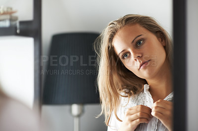 Buy stock photo A young woman getting dressed while looking in the mirror