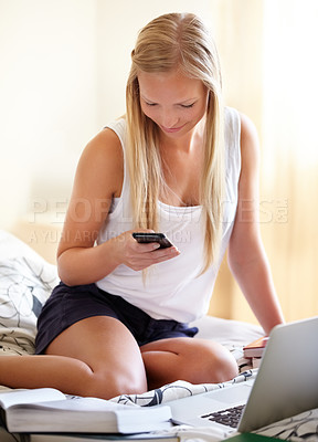 Buy stock photo Young college student working on an assignment at home while answering a text