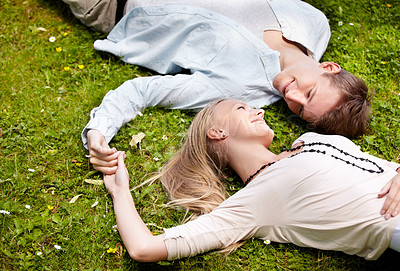 Buy stock photo Cute young couple lying together on the grass outside