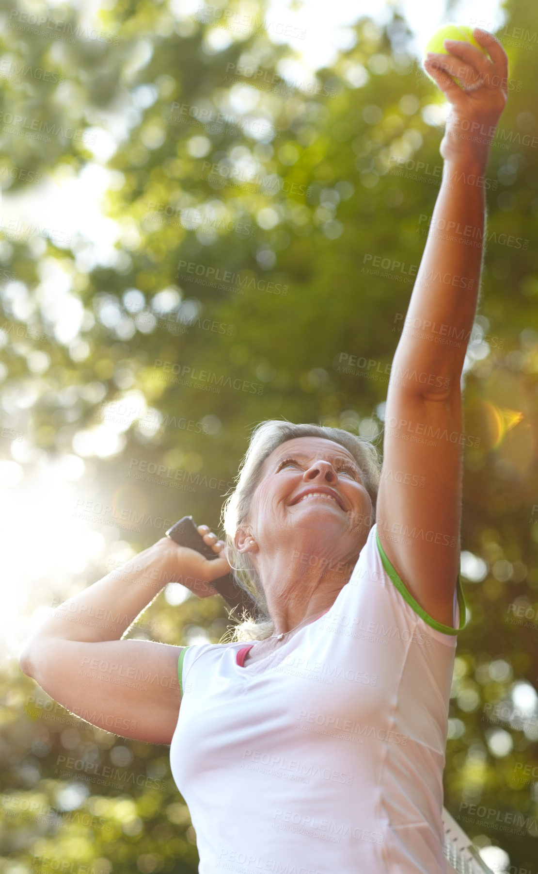 Buy stock photo Smiling senior woman lifting her arms in preparation for a tennis serve