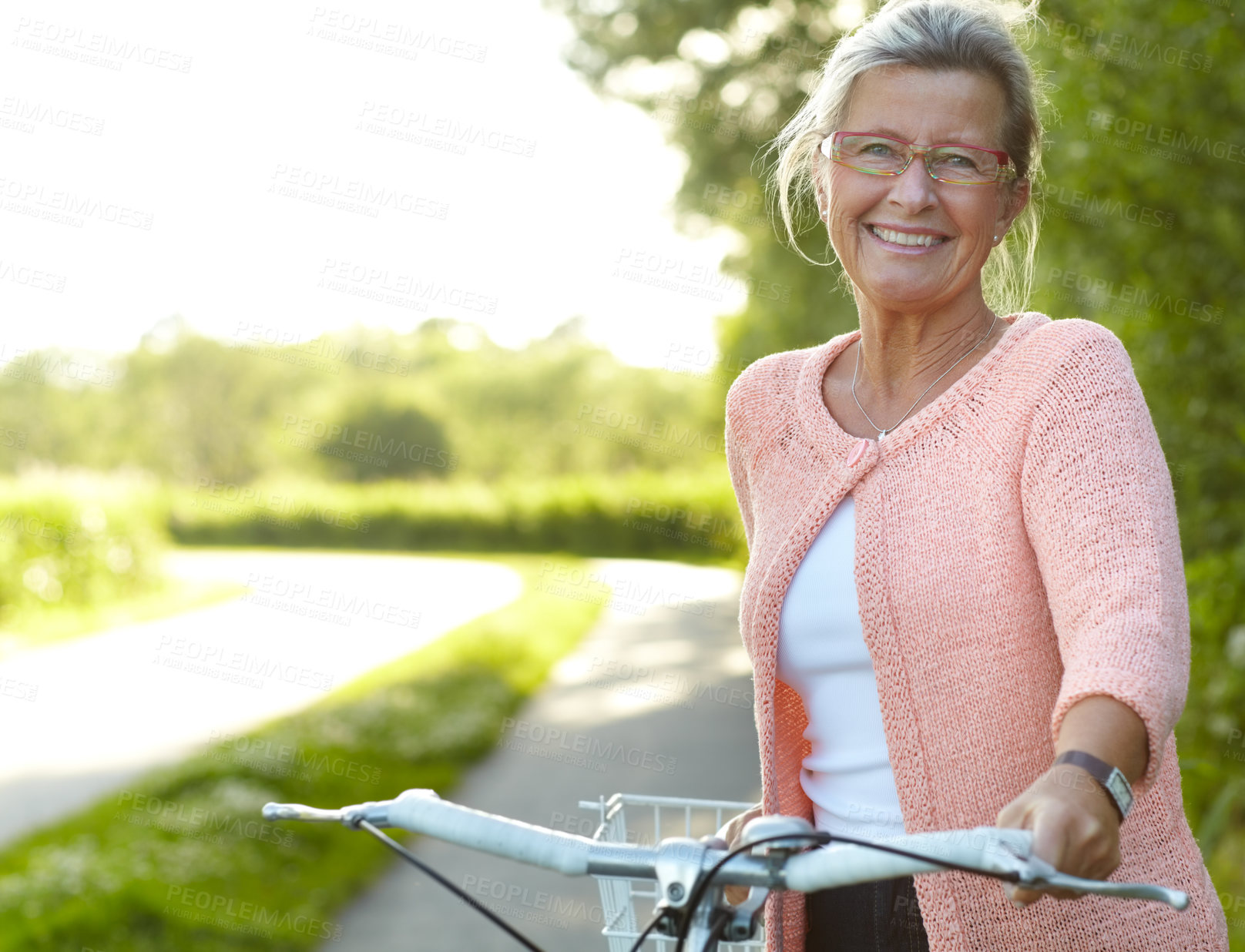 Buy stock photo Smiling senior woman standing on a country lane with her bicycle