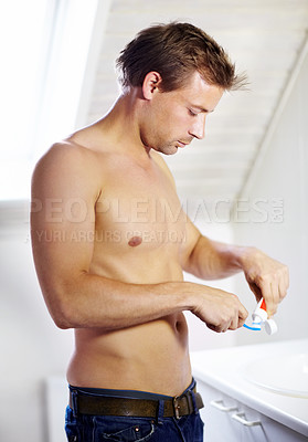 Buy stock photo Handsome young guy putting toothpaste on a toothbrush