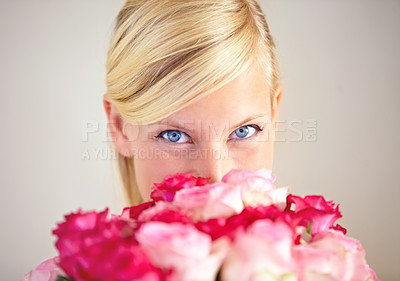 Buy stock photo Portrait of a young woman peering over a bouquet of pink roses