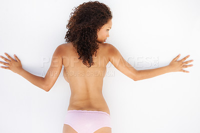 Buy stock photo Rear view of a topless young woman leaning against a wall with her arms spread out