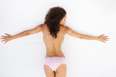 Buy stock photo Rear view of a topless young woman leaning against a wall with her arms spread out