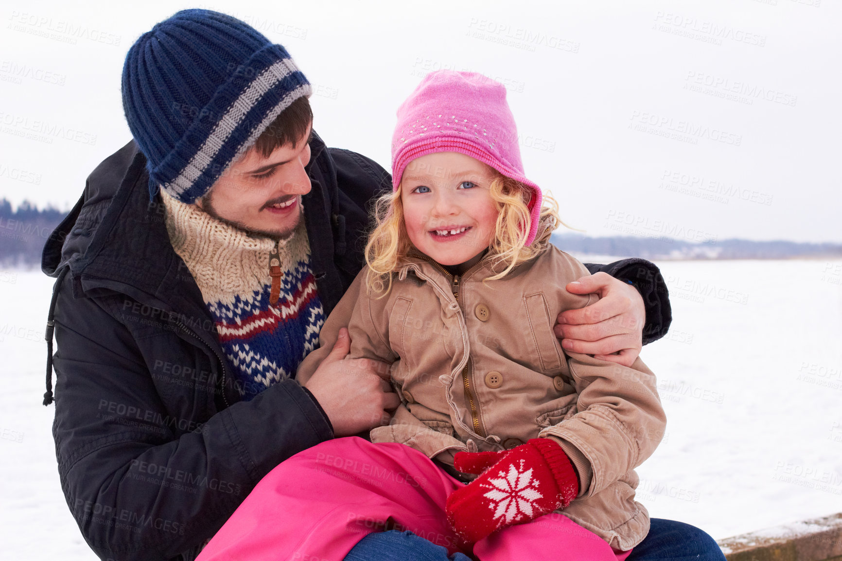 Buy stock photo Little girl sitting happily on her father's lap outside on a crisp winter's day