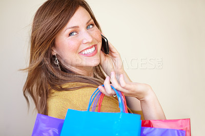Buy stock photo Cropped shot of a beautiful young woman talking on her cellphone while holding shopping bags