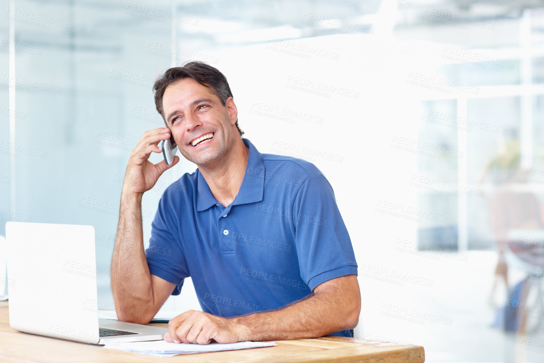 Buy stock photo Businessman, phone and smile for conversation in modern office with people, consultation or call for meeting. Male entrepreneur, mature and happy with technology, laptop and mobile for connectivity