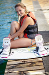 A pretty young girl sitting on a jetty next to a wakeboard