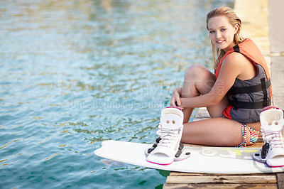 Buy stock photo Portrait of a pretty young girl sitting on a jetty next to a wakeboard