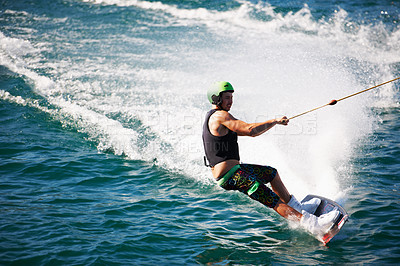 Buy stock photo A young man wearing a helmet and lifejacket wake boarding on a lake
