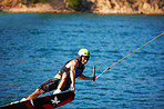 A young man wearing a helmut and lifejacket wakeboarding on a lake