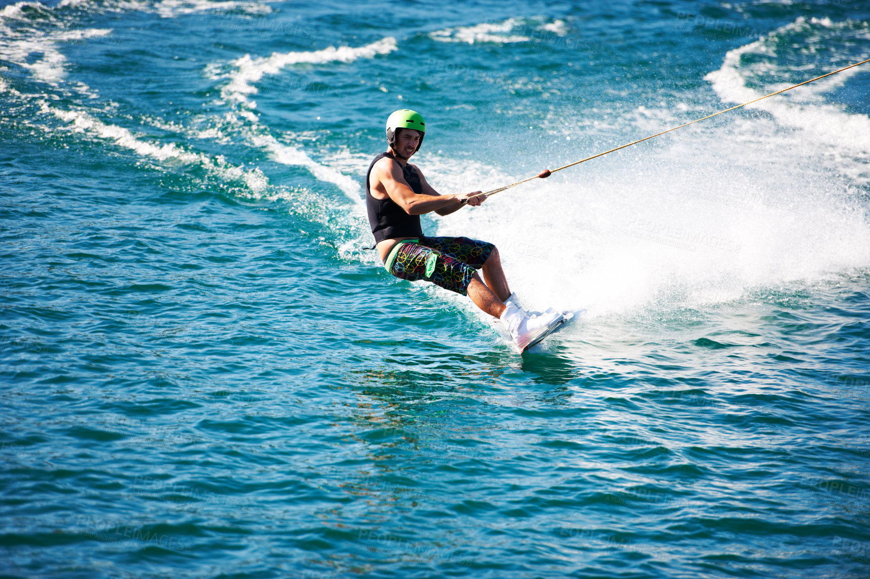 Buy stock photo A young man wearing a helmet and lifejacket wakeboarding on a lake