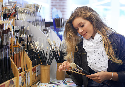 Buy stock photo Shot of a young female artist shopping for paint brushes in an art store 