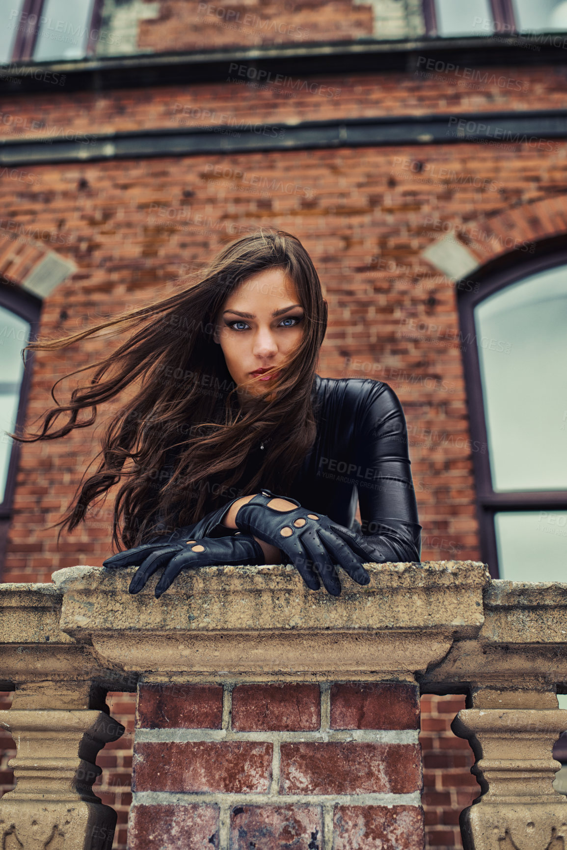 Buy stock photo Seductive young woman in a black catsuit looking at you from a rooftop