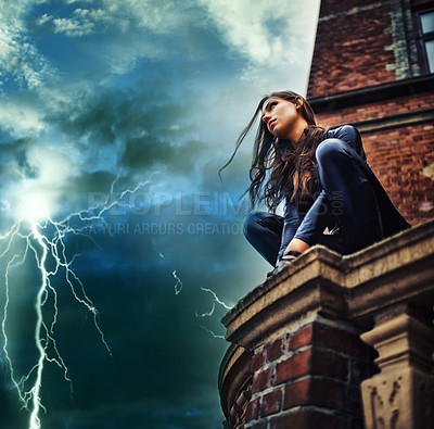 Buy stock photo Seductive young woman in a black catsuit crouched on a rooftop in a lightening storm