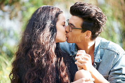 Buy stock photo Cute young couple sitting outside sharing a romantic kiss