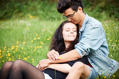 Buy stock photo Young couple sitting together affectionately in a springtime field