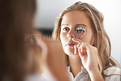 Buy stock photo A teenage girl curling her eyelashes in the mirror
