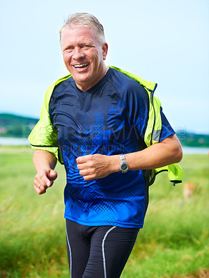 Buy stock photo Portrait, senior or happy man running in nature with smile, fitness or energy outdoors for exercise. Laughing, wellness or healthy mature runner on jog for cardio training or workout on grass in park