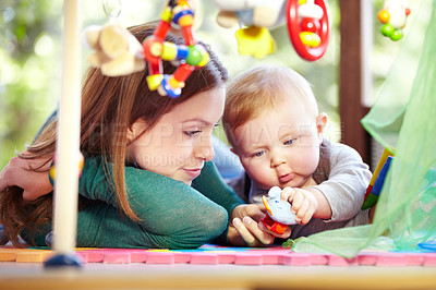 Buy stock photo Cute young mom lying alongside her infant son on the playroom floor