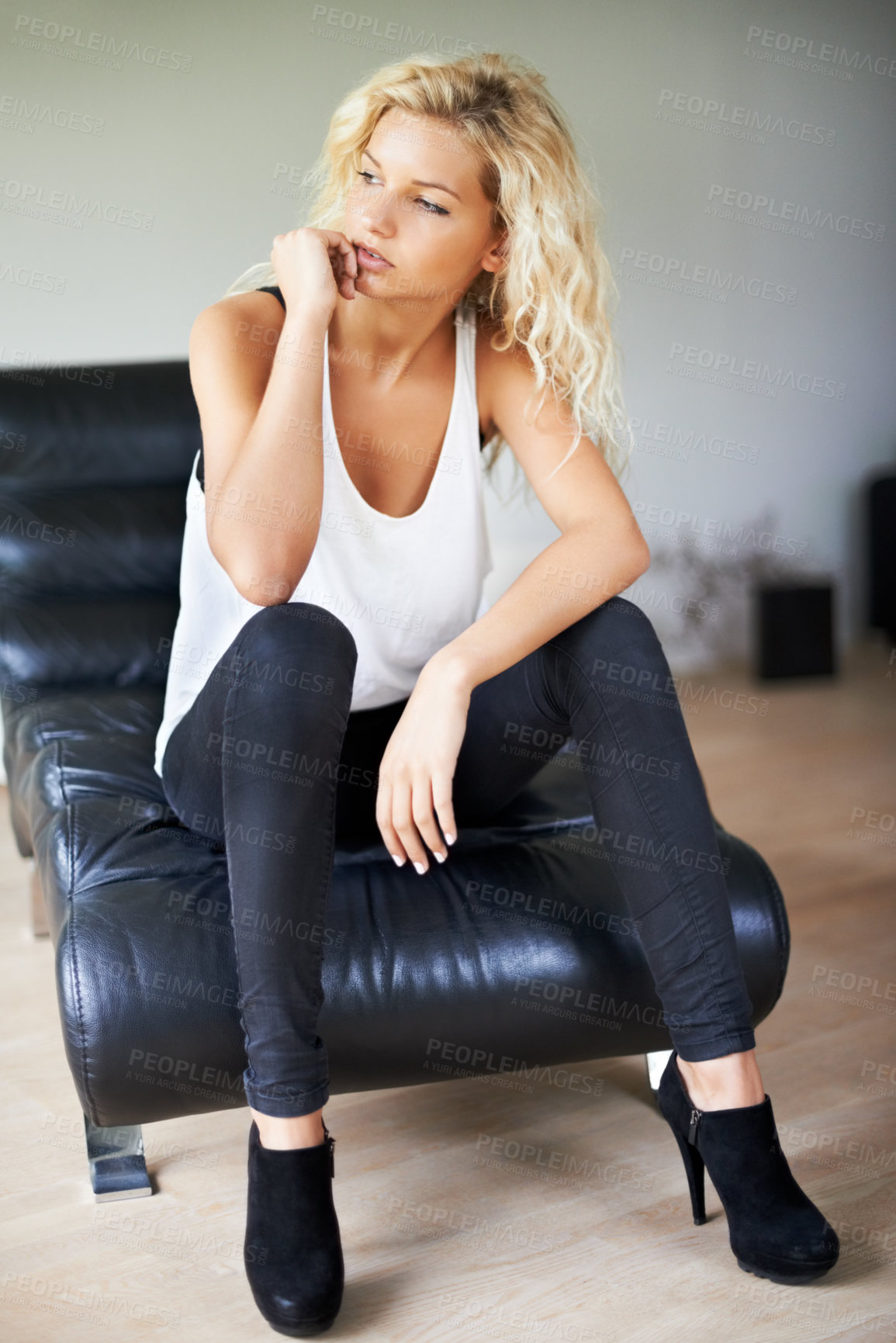 Buy stock photo Beautiful young blonde sitting on a modern black leather chair