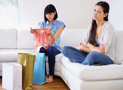 Buy stock photo A woman looking away with disappointment while her friend is going through some new clothes she just bought