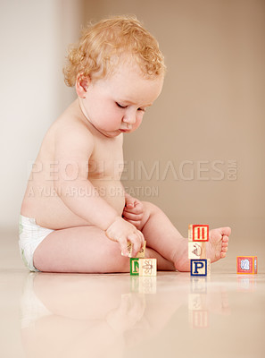 Buy stock photo Cute little baby sitting on the ground and playing with some alphabet blocks