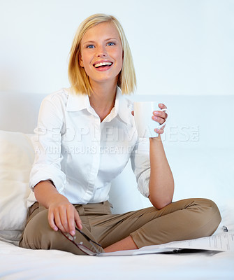 Buy stock photo A young woman working on her bed while drinking coffee